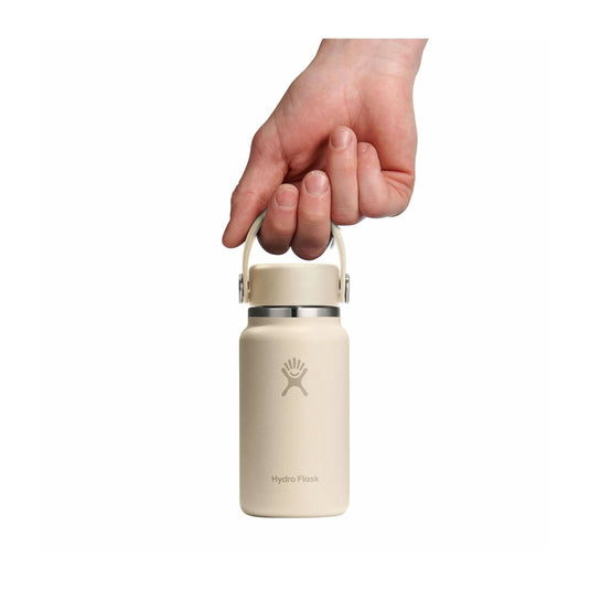 Beige Hydro Flask bottle held by a hand on a white background