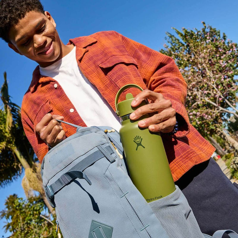Load image into Gallery viewer, A man outdoors wearing an orange plaid shirt and white t-shirt, holding a green Hydro Flask bottle inside a light blue-gray backpack.
