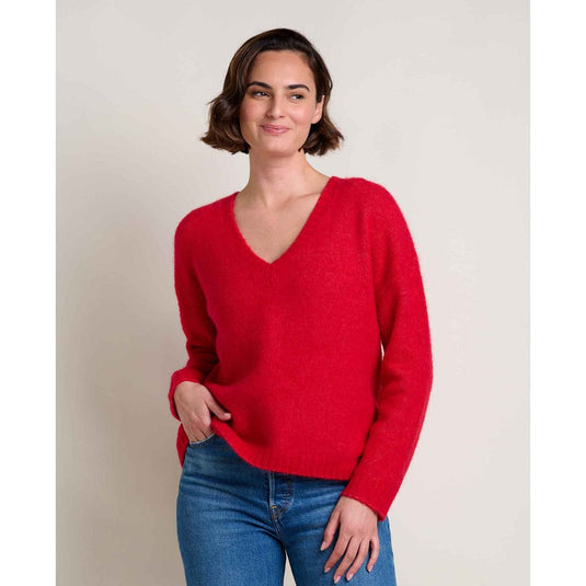 Woman wearing a red sweater and blue jeans against a plain background
