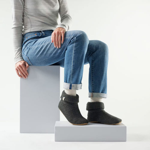 Person wearing gray slippers sitting on a white block with a plain background