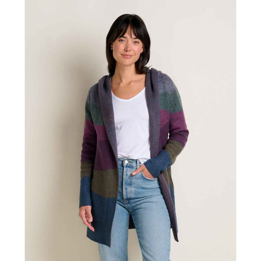 Woman wearing a colorful cardigan over a white shirt and blue jeans on a plain background