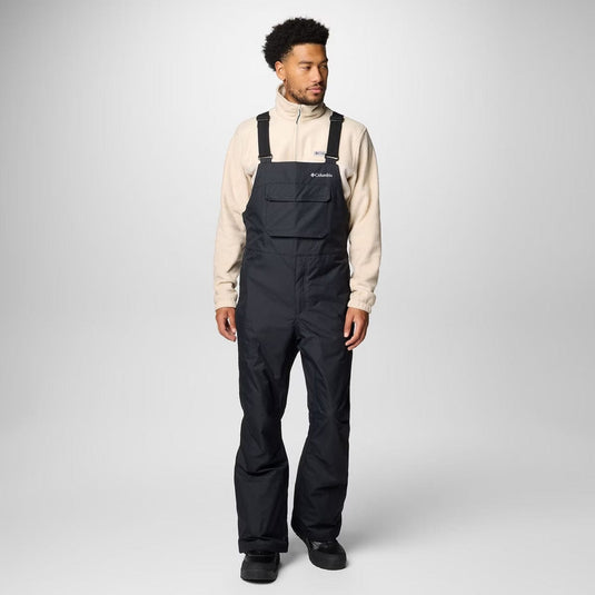 Person wearing black bib overalls with a beige jacket on a white background