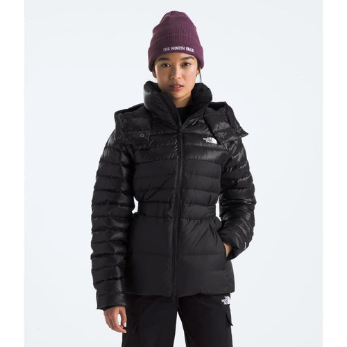 A woman wearing a black The North Face winter jacket with a hood, black pants, and a purple beanie.