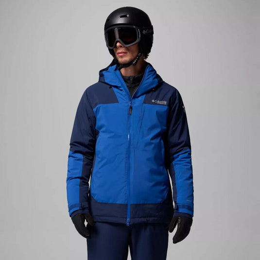 Person wearing a blue and navy ski jacket with a helmet and goggles on a gray background