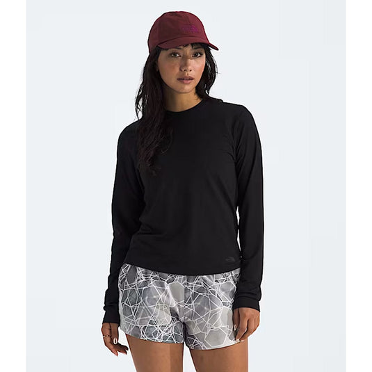 Woman wearing a black long-sleeve shirt, maroon cap, and patterned shorts on a white background