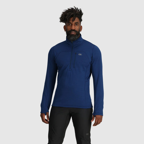 Man wearing a blue pullover with a brand logo on a gray background
