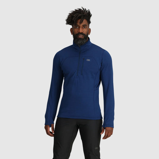 Man wearing a blue pullover with a brand logo on a gray background
