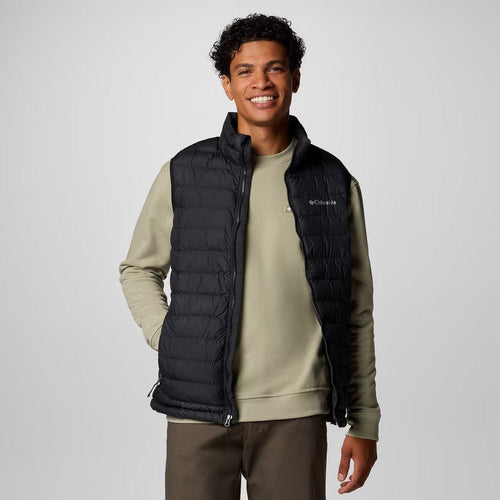 Man wearing a black puffer vest over a green sweater on a white background