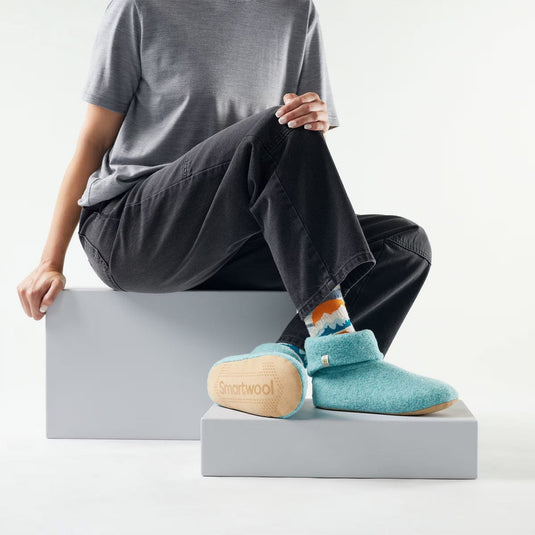 Person wearing teal Slumberfootz slippers with a visible brand logo on a white background