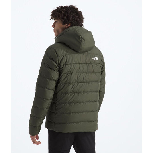 Person wearing a green puffer jacket with a brand logo on a white background