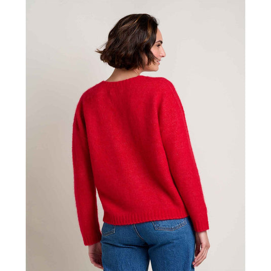 Woman wearing a red sweater and blue jeans against a plain background