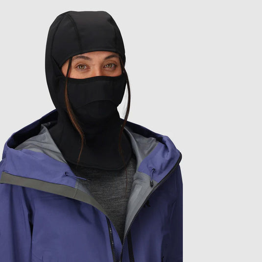 Person wearing a black hooded face mask and blue jacket on a light gray background