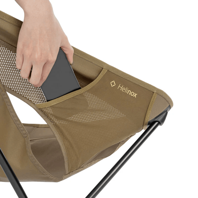 Load image into Gallery viewer, Brown camping chair with a person placing a phone into a pocket, branded 'Helinox'.
