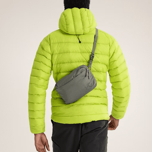 Person wearing a bright green puffer jacket with a gray crossbody bag on a beige background