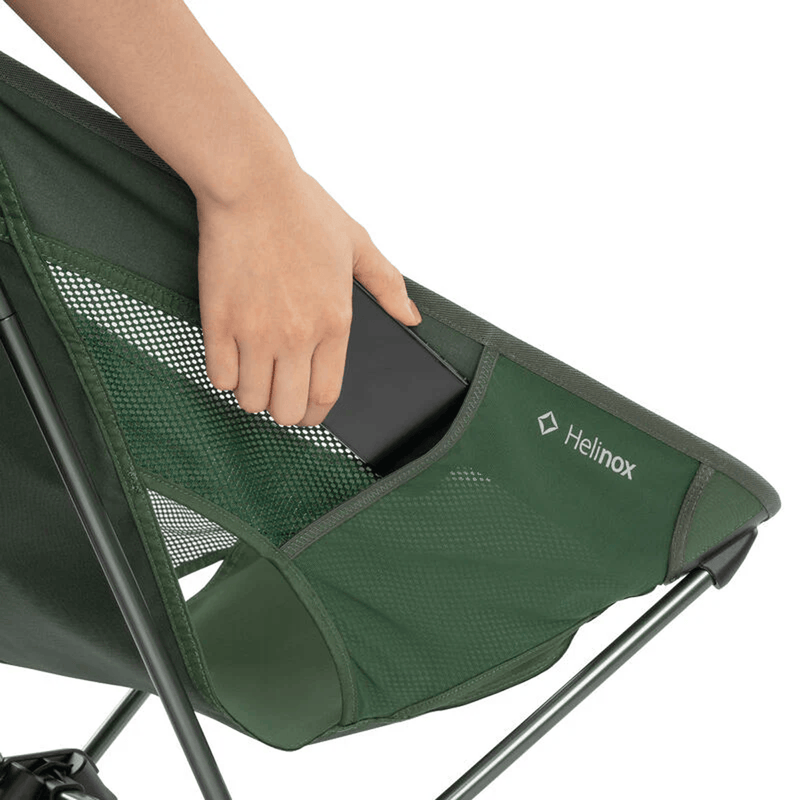 Load image into Gallery viewer, Green camping chair with a person's hand holding a phone, featuring the Helinox logo.
