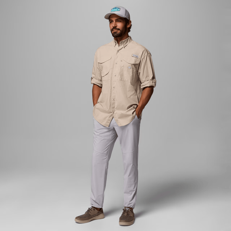Load image into Gallery viewer, Man wearing a beige shirt and light gray pants with a cap on a gray background
