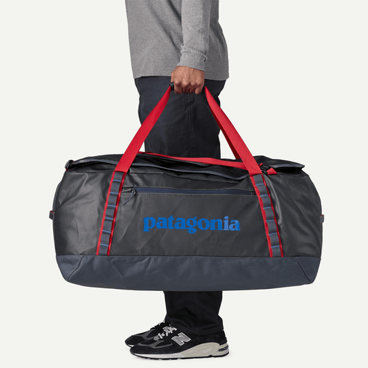 Person holding a Patagonia duffel bag with red straps on a light gray background