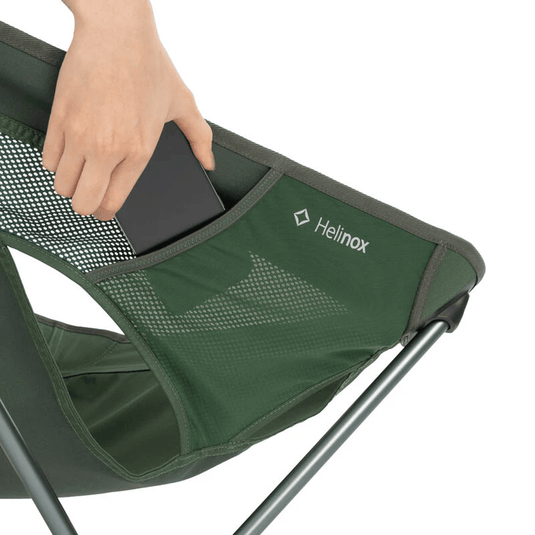 Green camping chair with a hand placing an item into a pocket, featuring the Helinox logo.